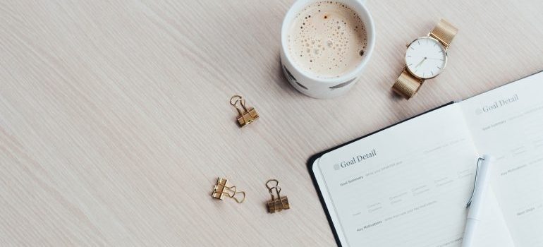 A cup of coffee next to a notebook, representing working on your moving timeline.