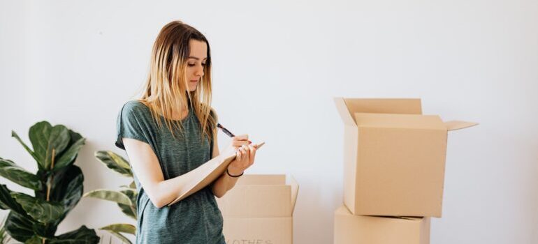 A woman standing near cardboard boxes and writing something down.