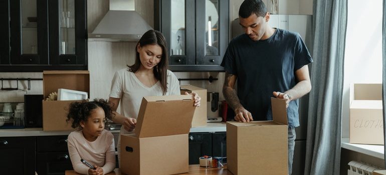 A man, woman, and a child are packing items into cardboard boxes.