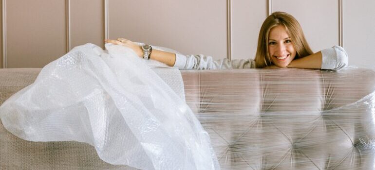 A woman smiling next to a wrapped couch.