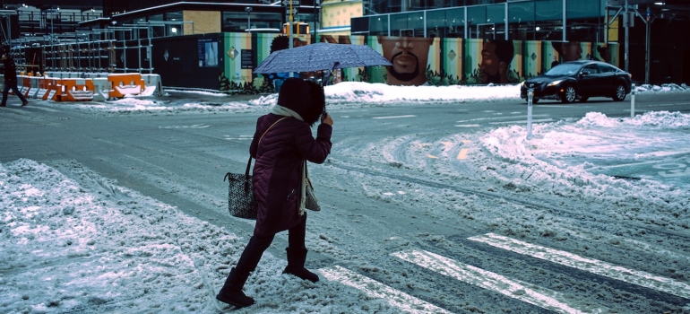 a woman in winter clothing and an umbrella crossing the street full of snow