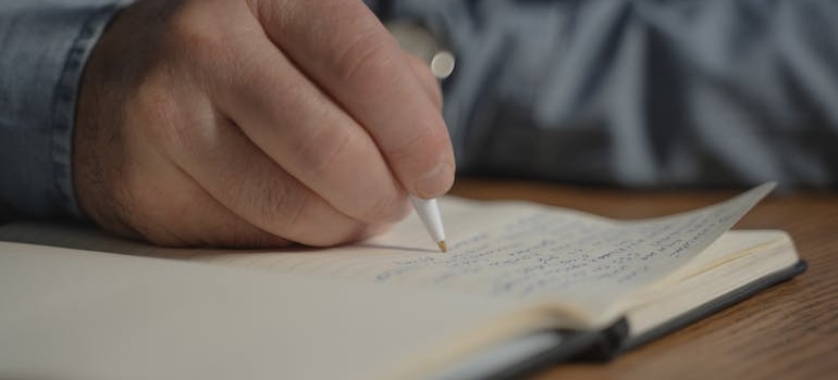 A person writing in a notebook a plan for moving next door.